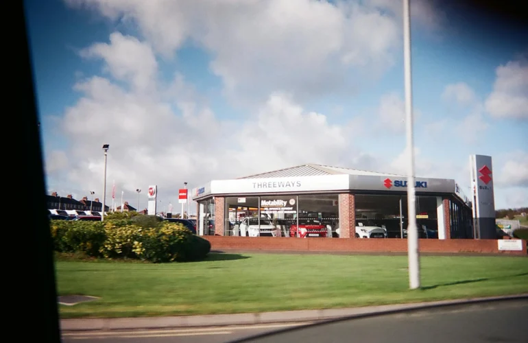 Exterior view of a car dealership featuring Suzuki automobiles under a bright sky.