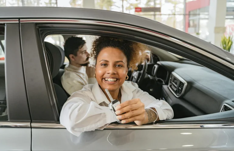 Joyful couple in their new car, holding keys in a dealership showroom, smiling warmly.